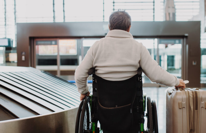 Rear view of man on wheelchair at airport with his luggage.